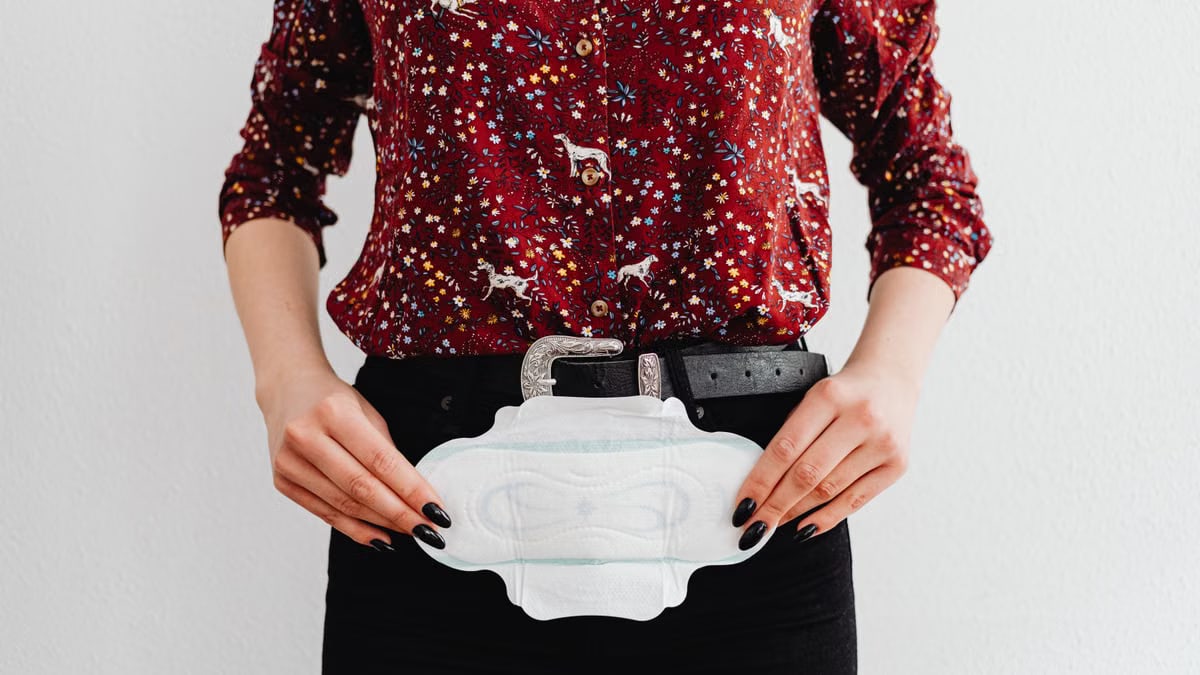 A woman in a colorful shirt holds a sanitary pad, symbolizing menstrual health awareness.