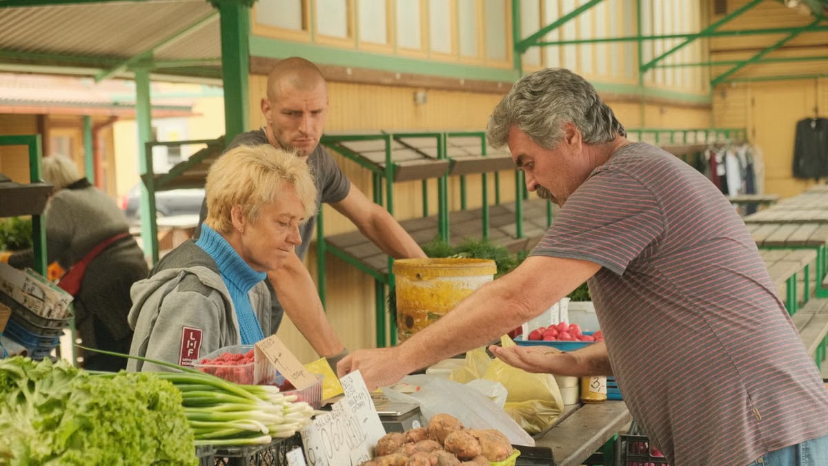 A farmer's market scene with vendors selling fresh produce including greens and potatoes.