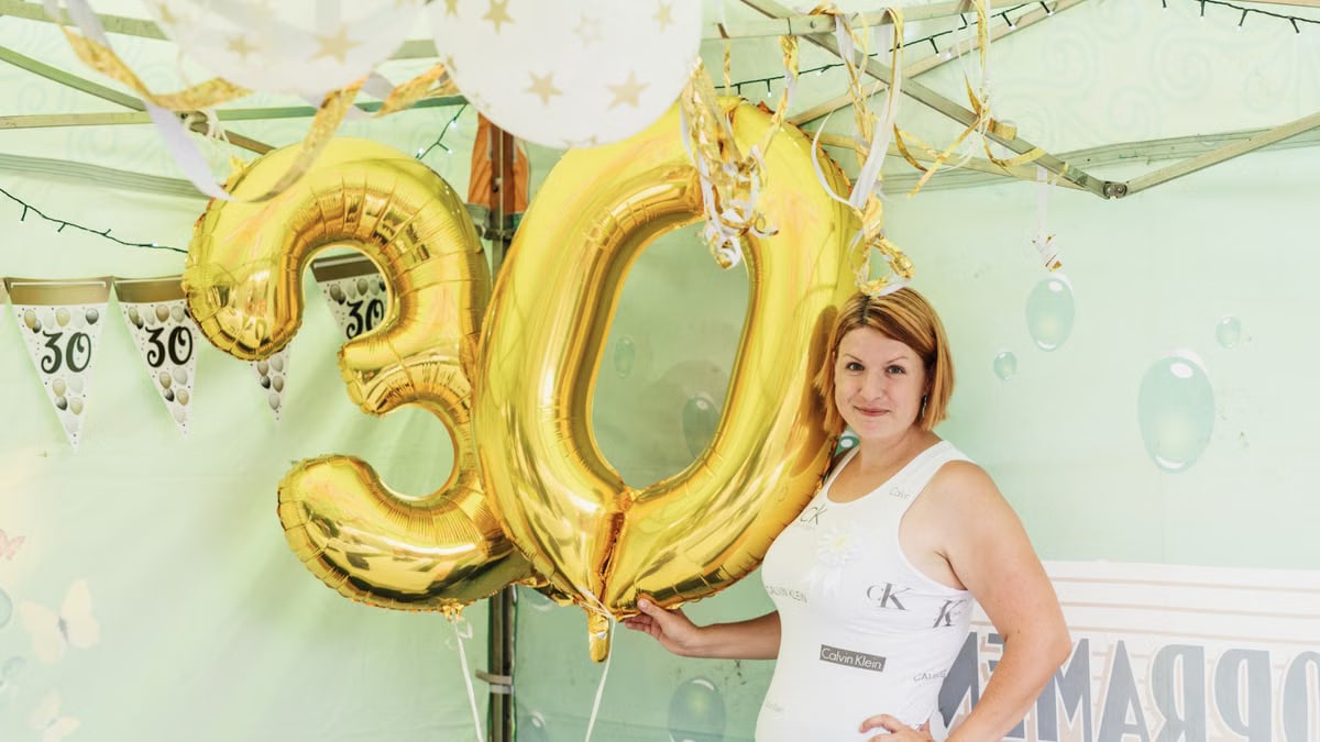 Woman posing with golden number 30 balloons at a birthday party celebration.